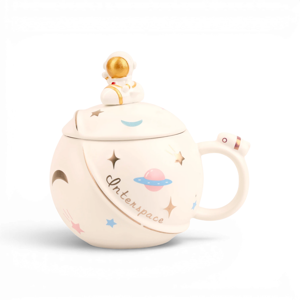 White ceramic mug with space-themed illustrations including planets, stars, and astronaut, topped with gold spaceman finial