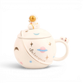 White ceramic mug with space-themed illustrations including planets, stars, and astronaut, topped with gold spaceman finial