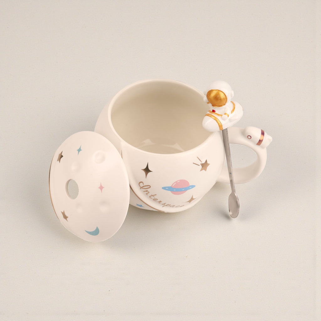 White ceramic mug with space-themed illustrations including astronaut, planet, and stars, matching lid and spoon