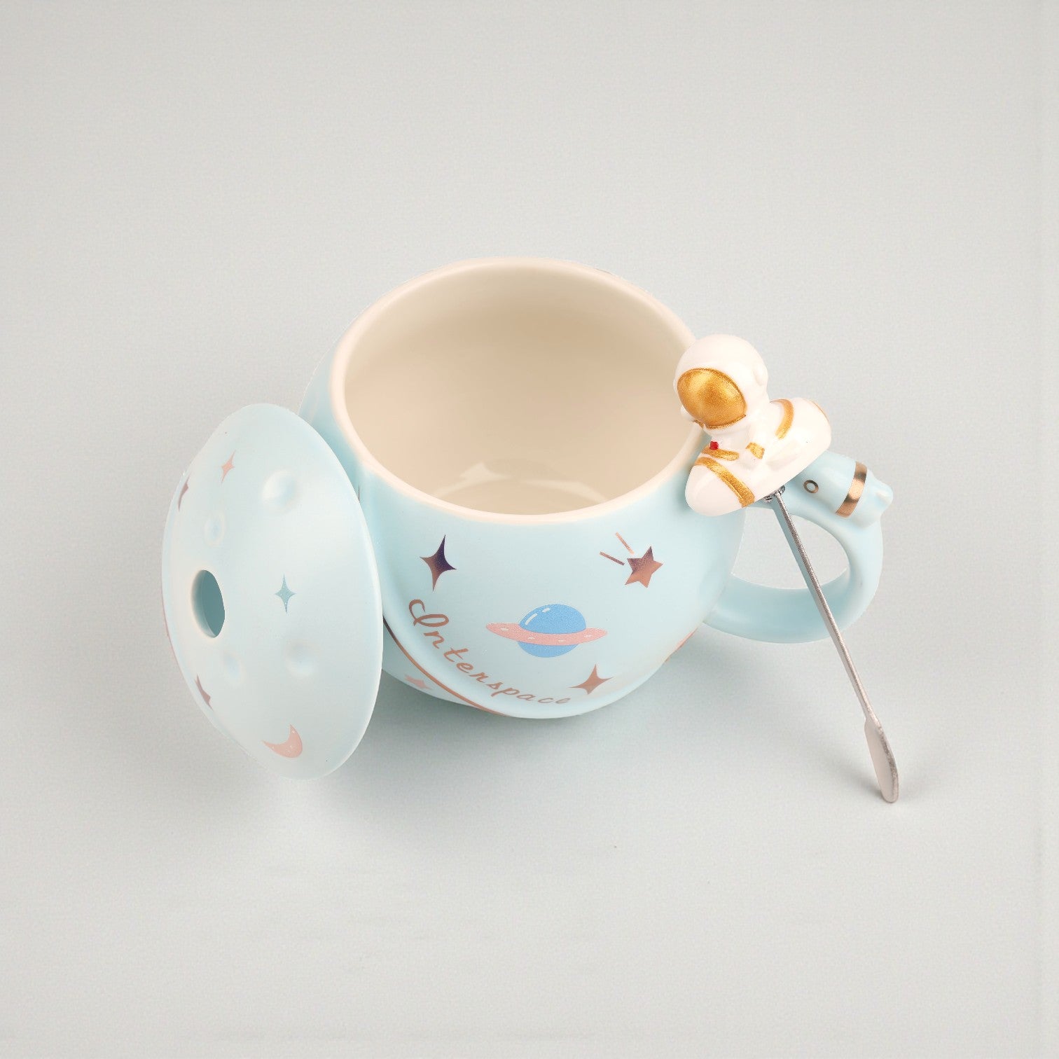 Light blue ceramic mug with space-themed illustrations, matching lid, and astronaut spoon with golden helmet