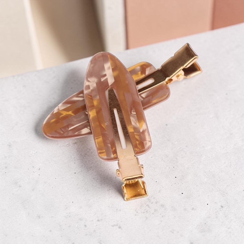 Tortoiseshell acrylic resin hair clips with gold-tone metal accents on white marble surface