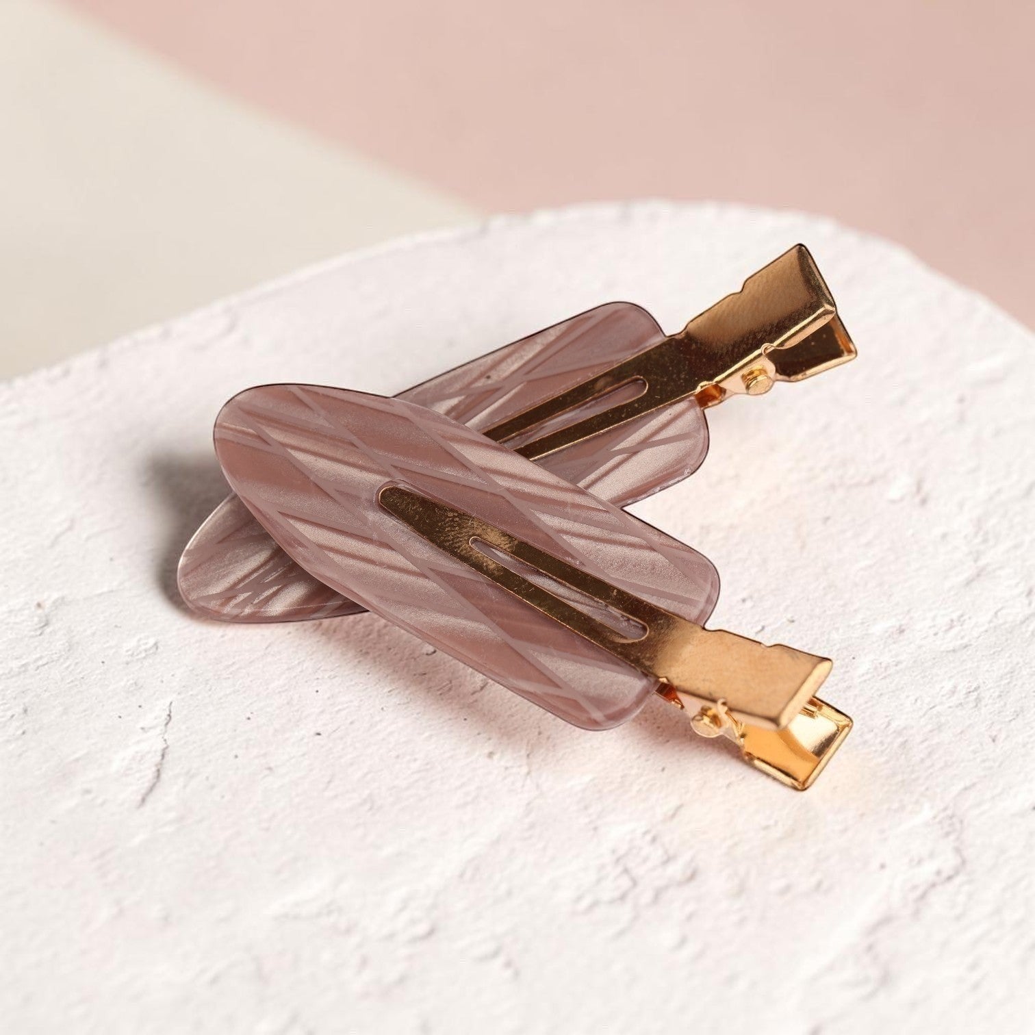 Mauve acrylic resin hair clips with gold-tone metal hardware on textured white surface