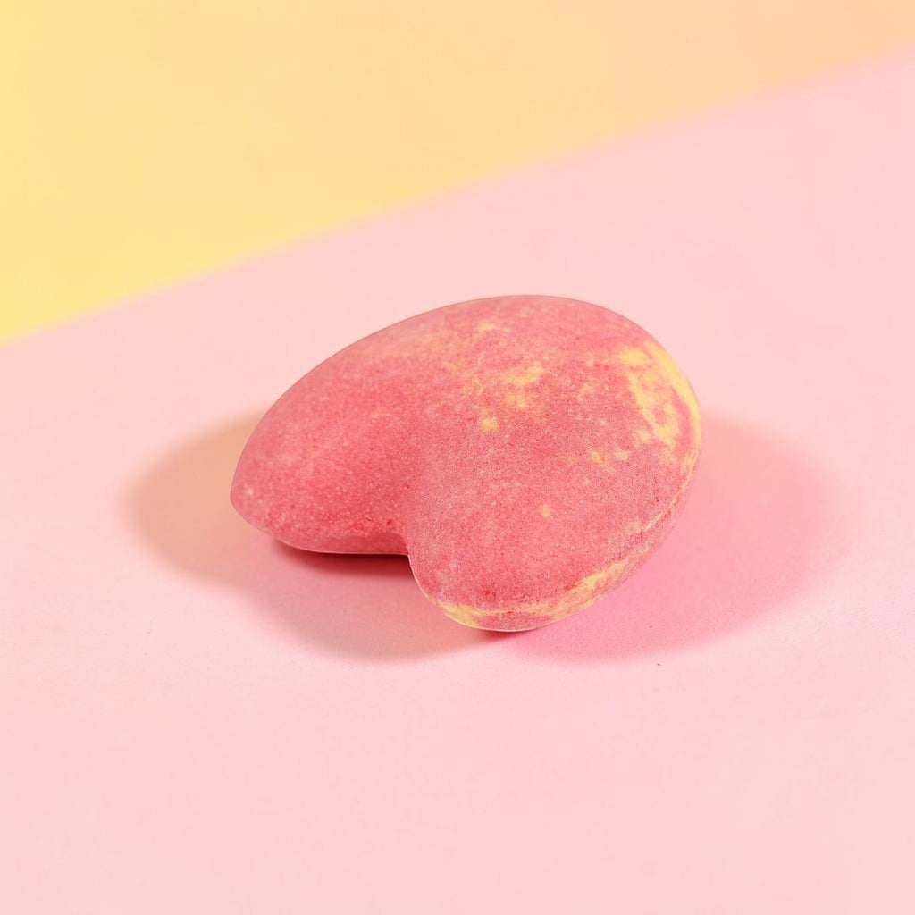 Pink heart-shaped bath bomb with gold shimmer accents on pastel background