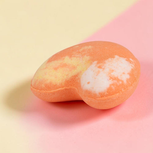 Peach-colored oval bath bomb with white swirl detail on pink and cream background