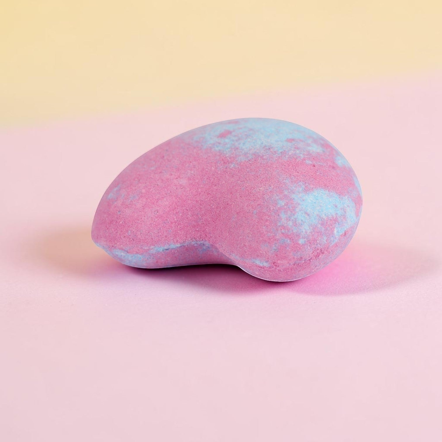 Pink and blue speckled oval bath bomb with fizzy texture on pastel background