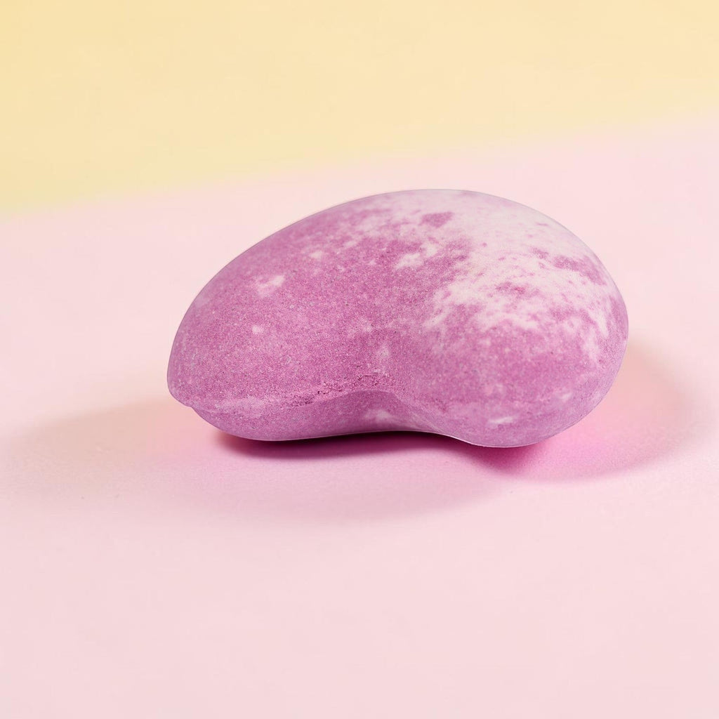Mauve fizzy bath bomb with speckled texture on pink background