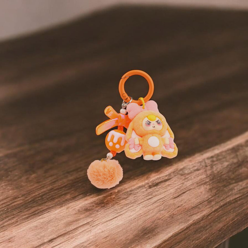 Llavero de conejo de peluche naranja de Boxigami con detalles de lazo rosa y pompón a juego. Diseño divertido.