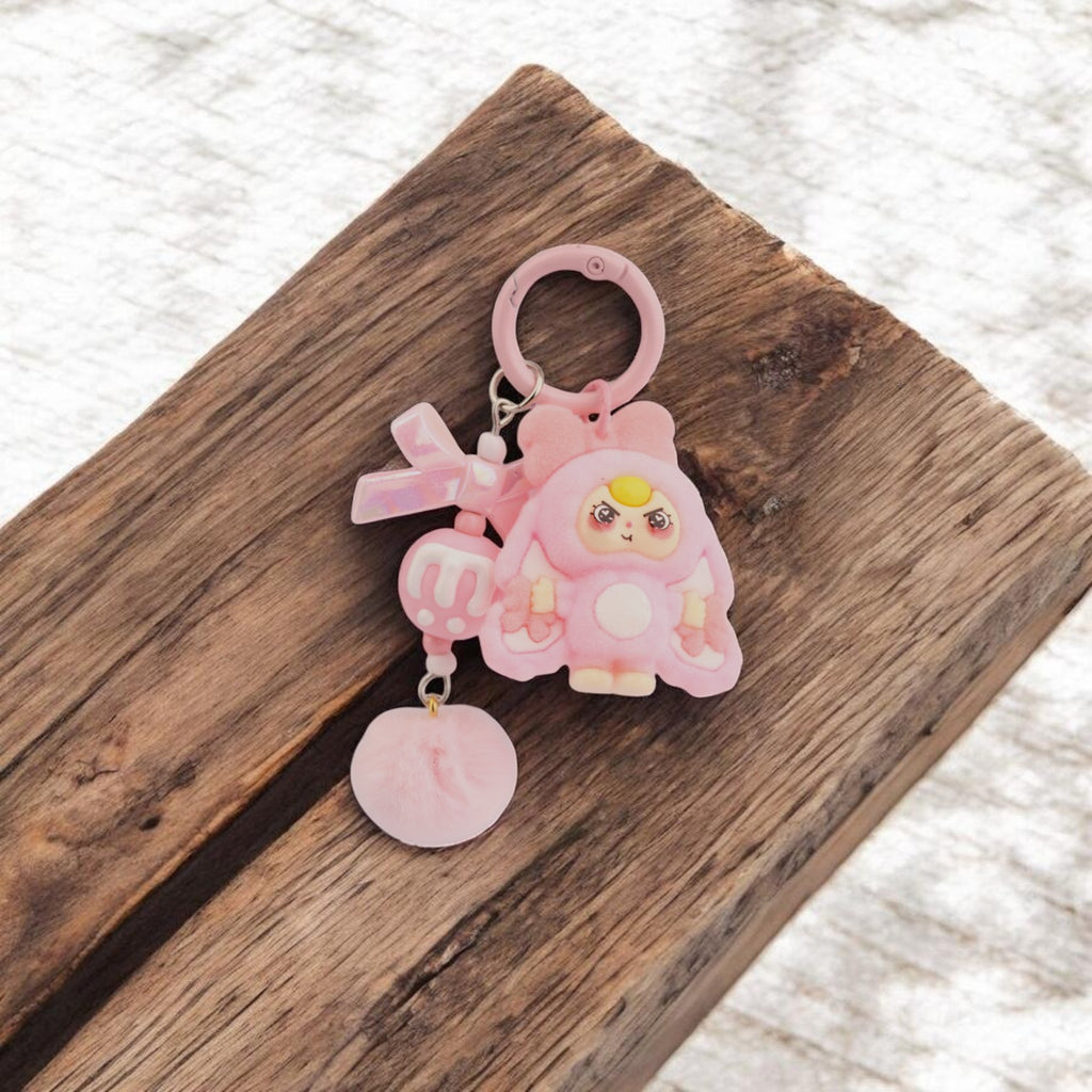 Boxigami llavero de conejo rosa con acabado afelpado, lazo brillante y pompón de pelo. Diseño divertido para bolsos y mochilas.